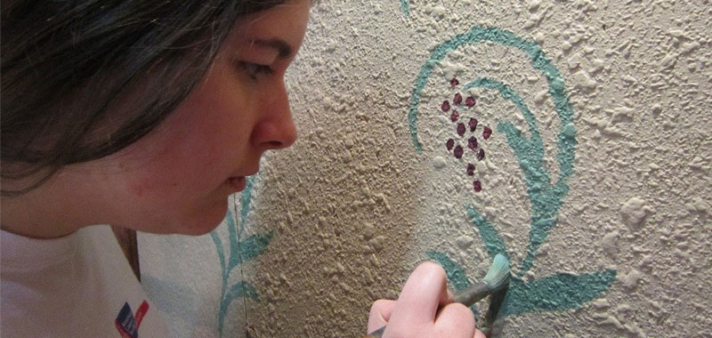 Young girl painting blue swirls on wall